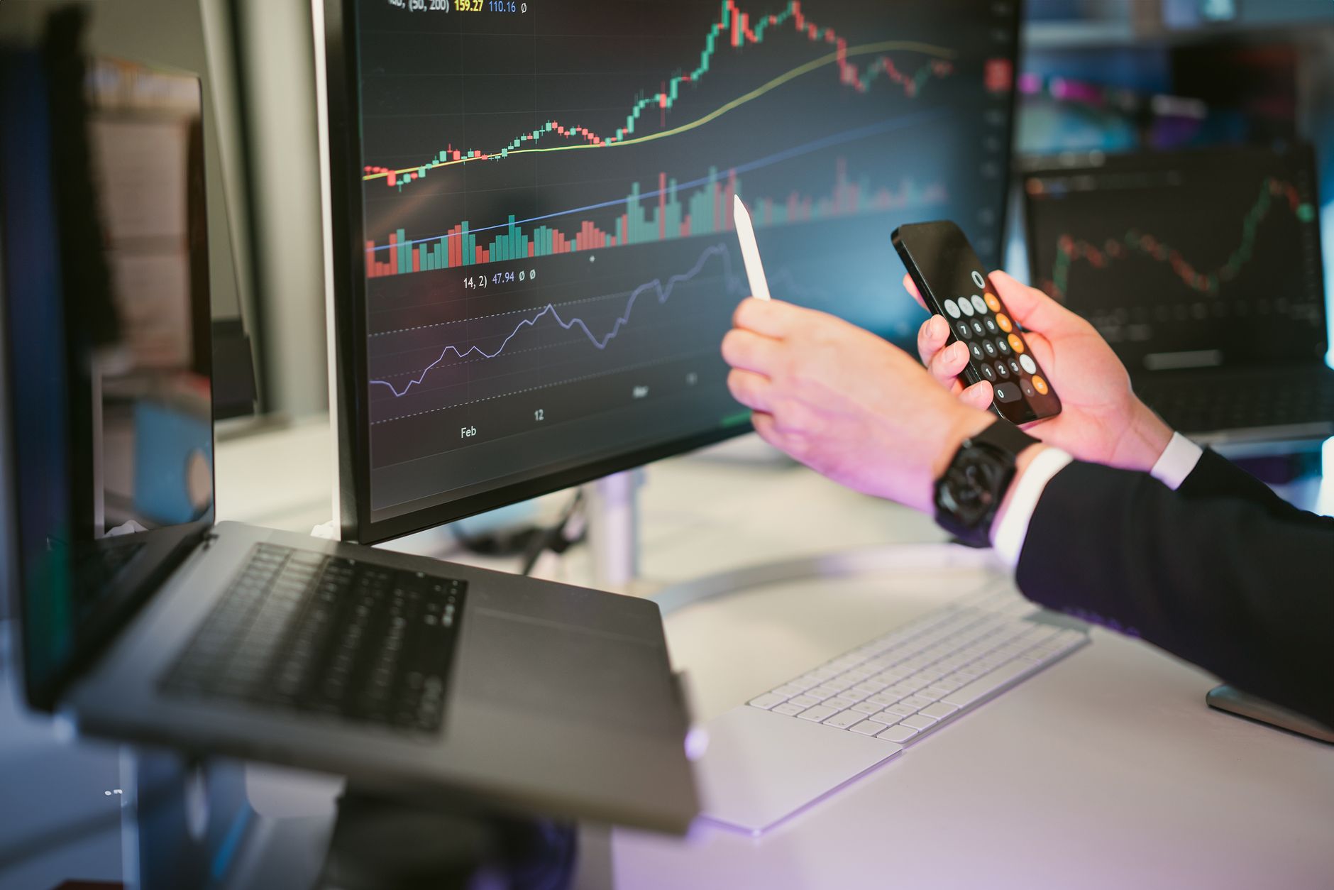 A professional analyzing financial charts on computer monitors and a smartphone, symbolizing digital finance strategies.