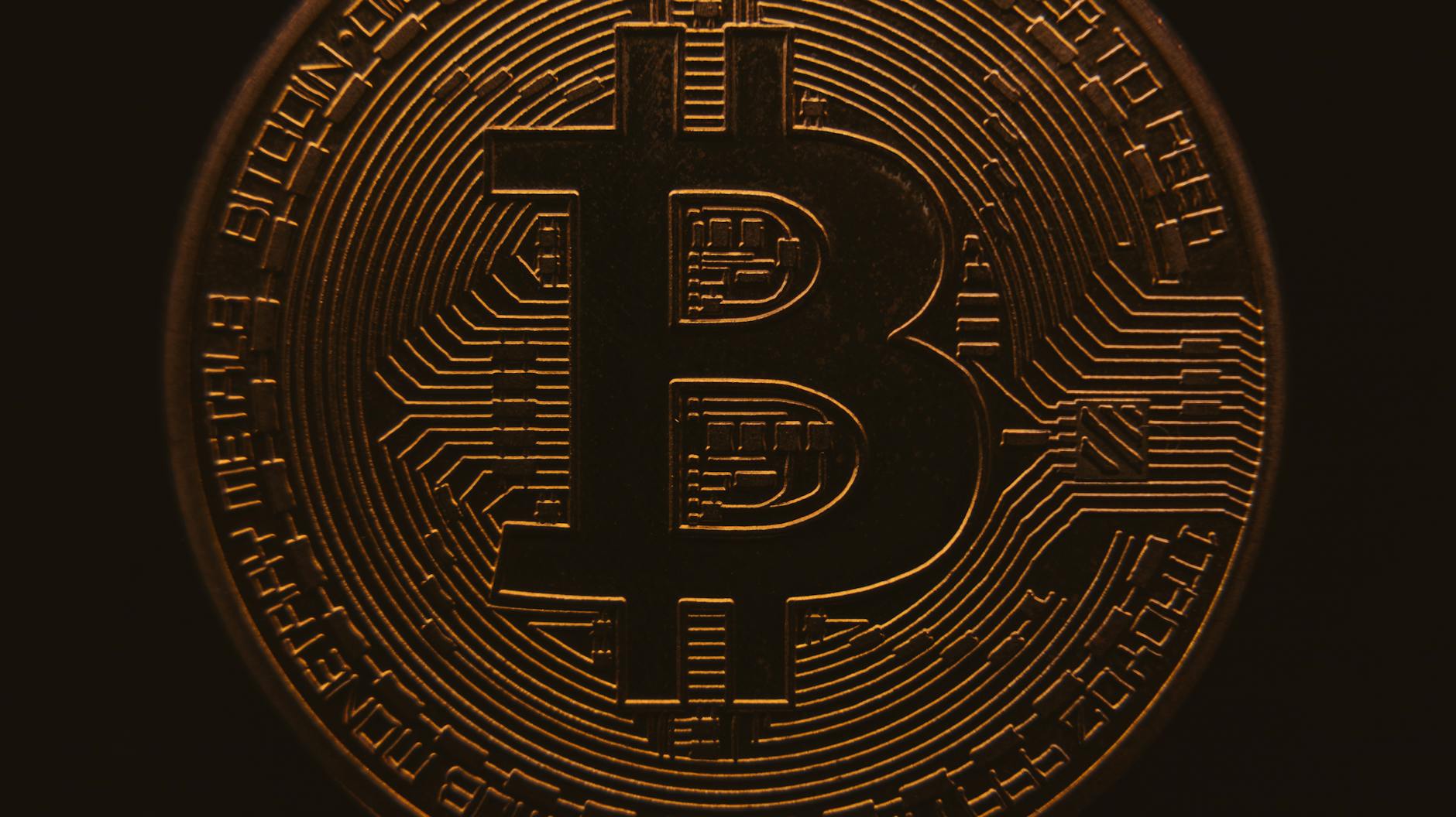 Close-up view of a bitcoin coin showing its intricate, digital design in a warm, dark ambiance.