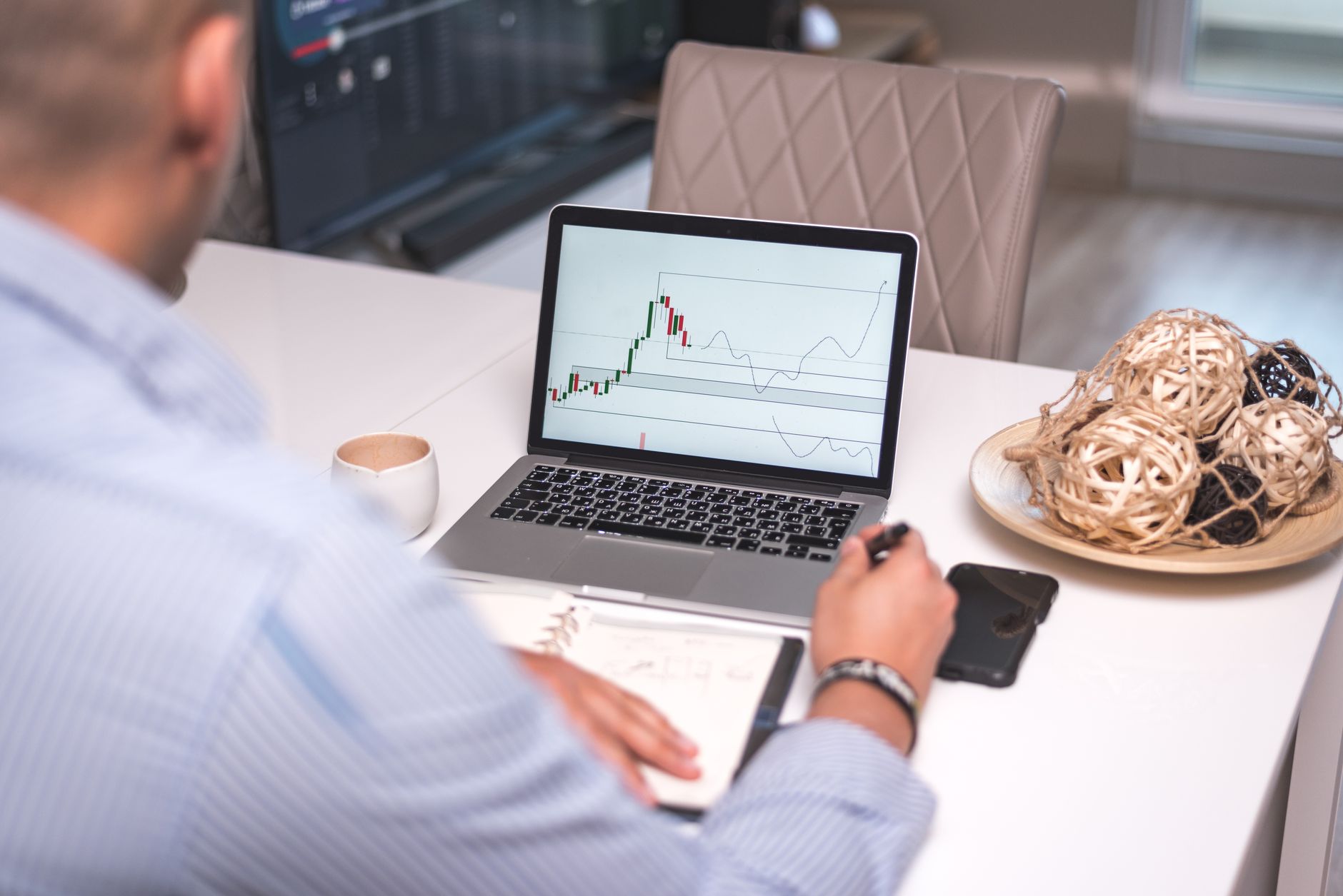 Man studies financial graphs on a laptop at a modern home office setting, focusing on market analysis.