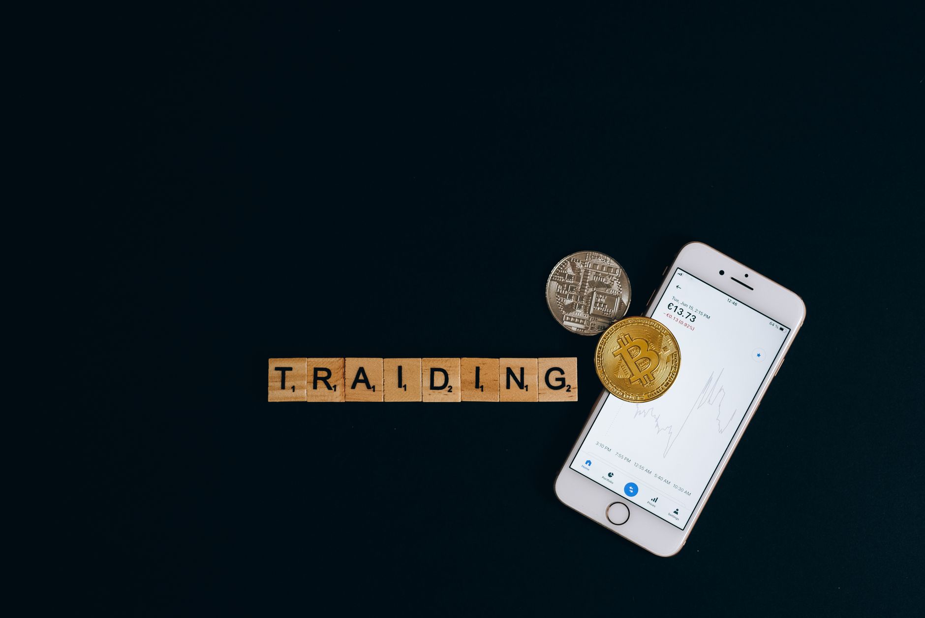 A smartphone and Bitcoin coins with trading letters on black background.