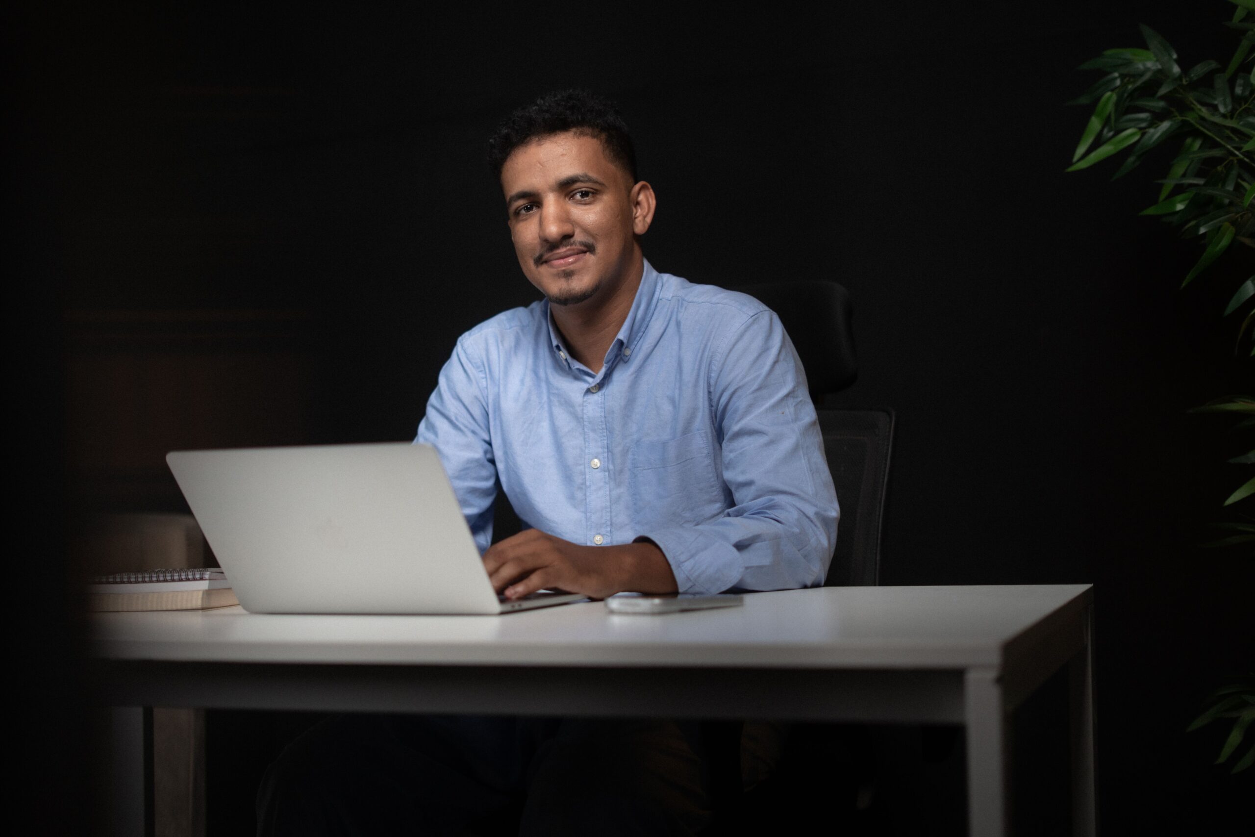Smiling businessman sitting at desk with laptop, ideal for corporate themes.