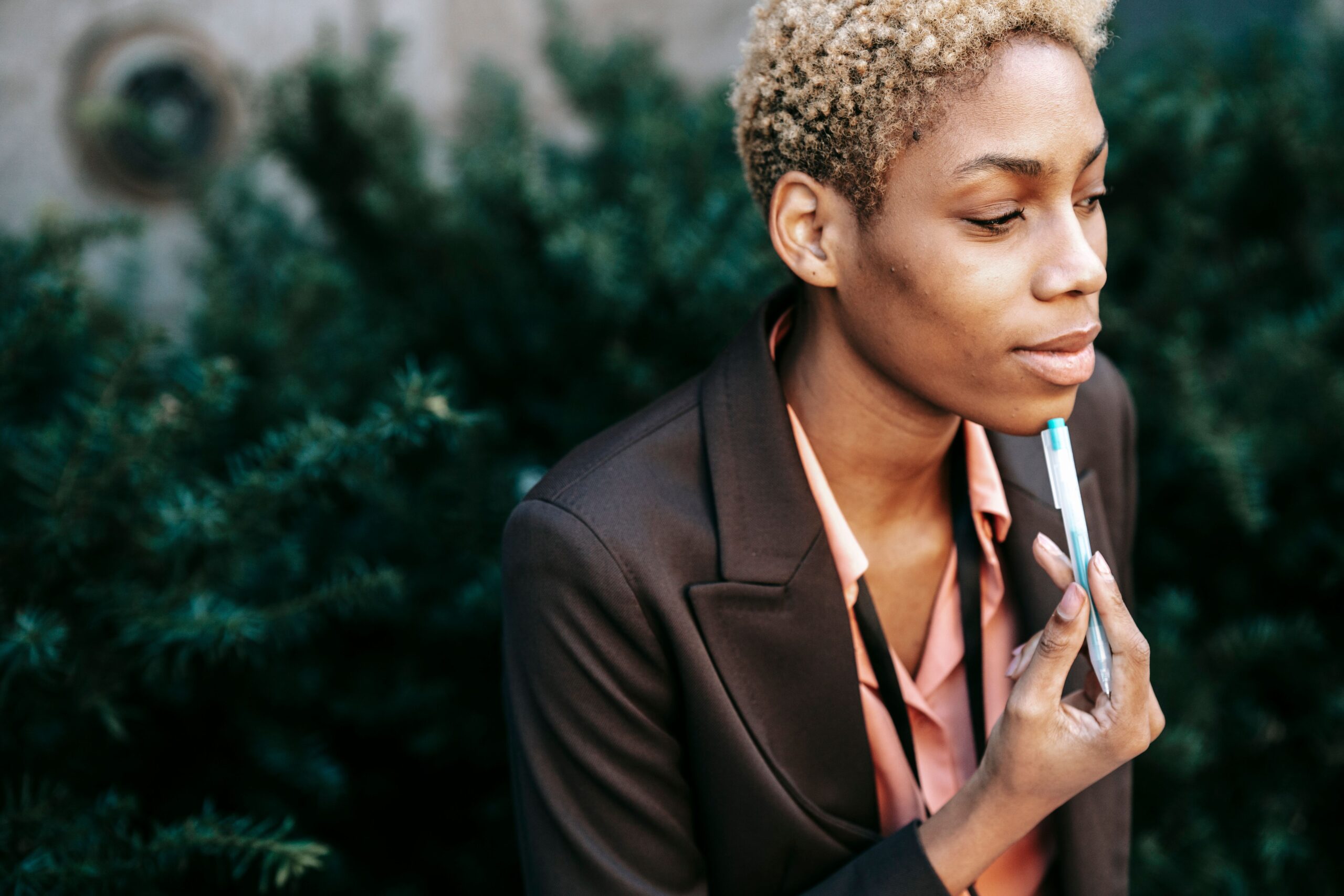 High angle of crop African American female entrepreneur in formal suit touching chin with pen while thinking about business