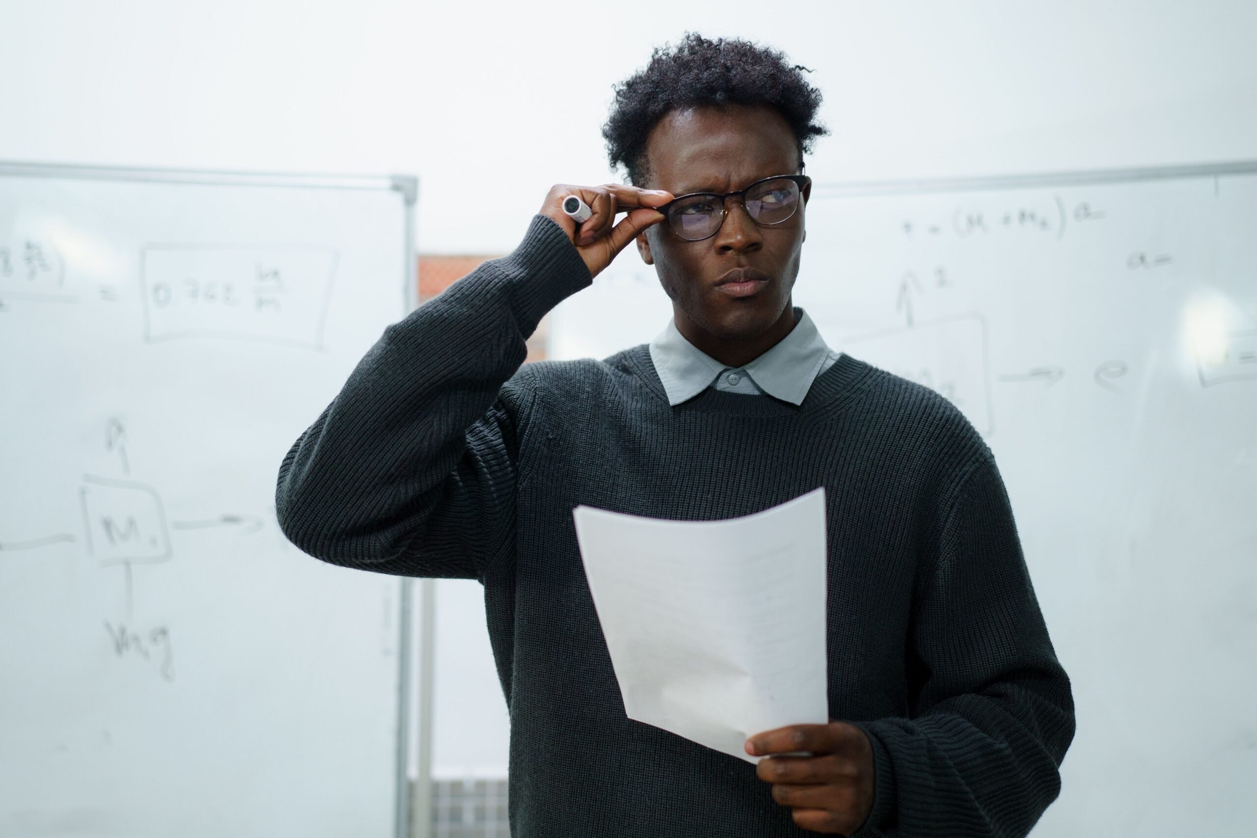 Focused businessman reading documents in an office setting with whiteboards.