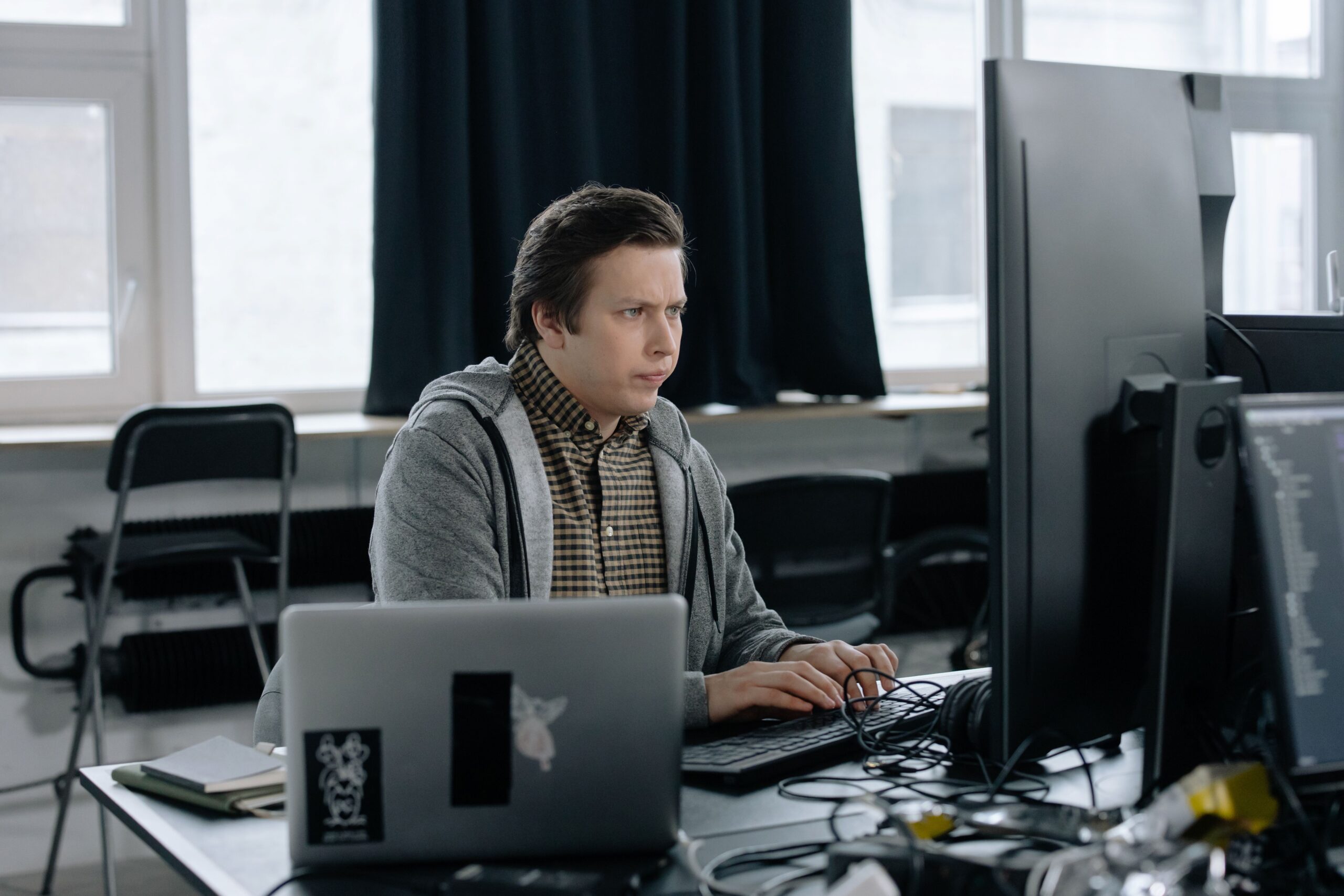 A dedicated programmer focused on coding at his workspace with dual monitors in a modern office setting.