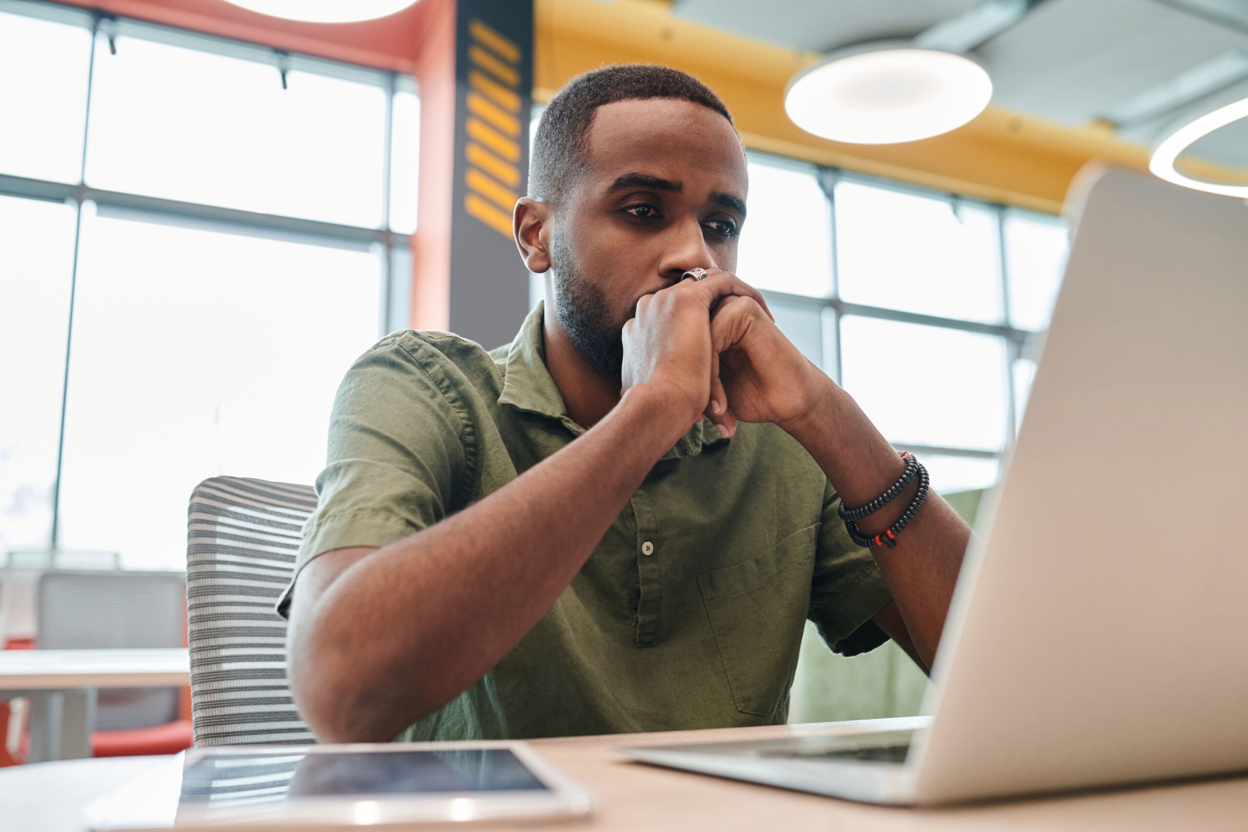 Thoughtful professional working on a laptop in a bright, modern office environment.