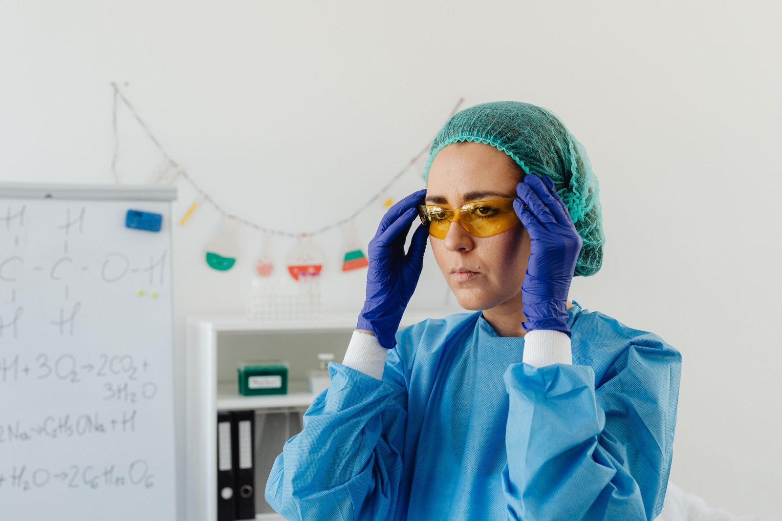 Woman scientist in protective gear adjusting goggles in a laboratory setting, focusing on preparation.