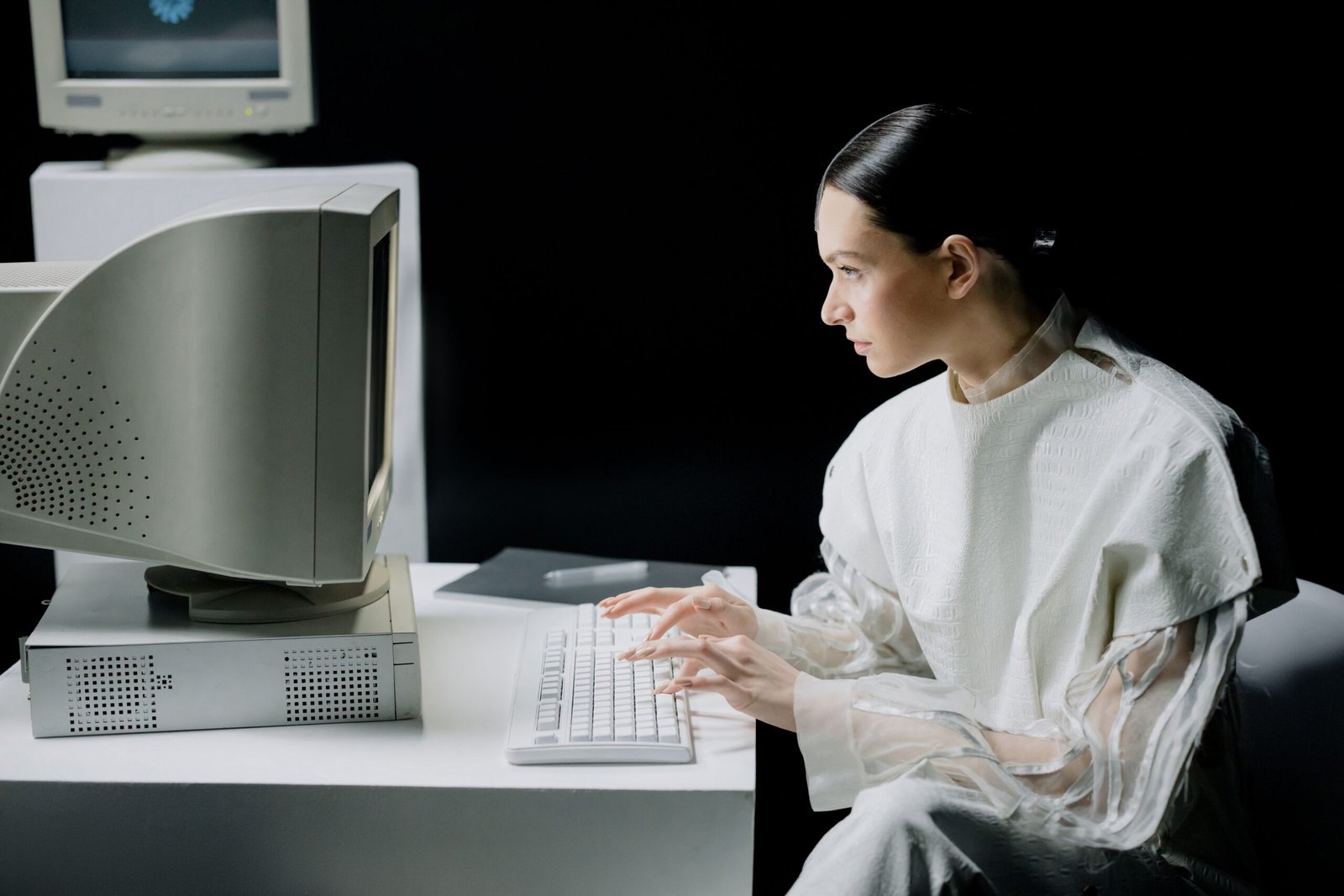 A woman in modern attire using a vintage computer in a dark setting, blending past and future.