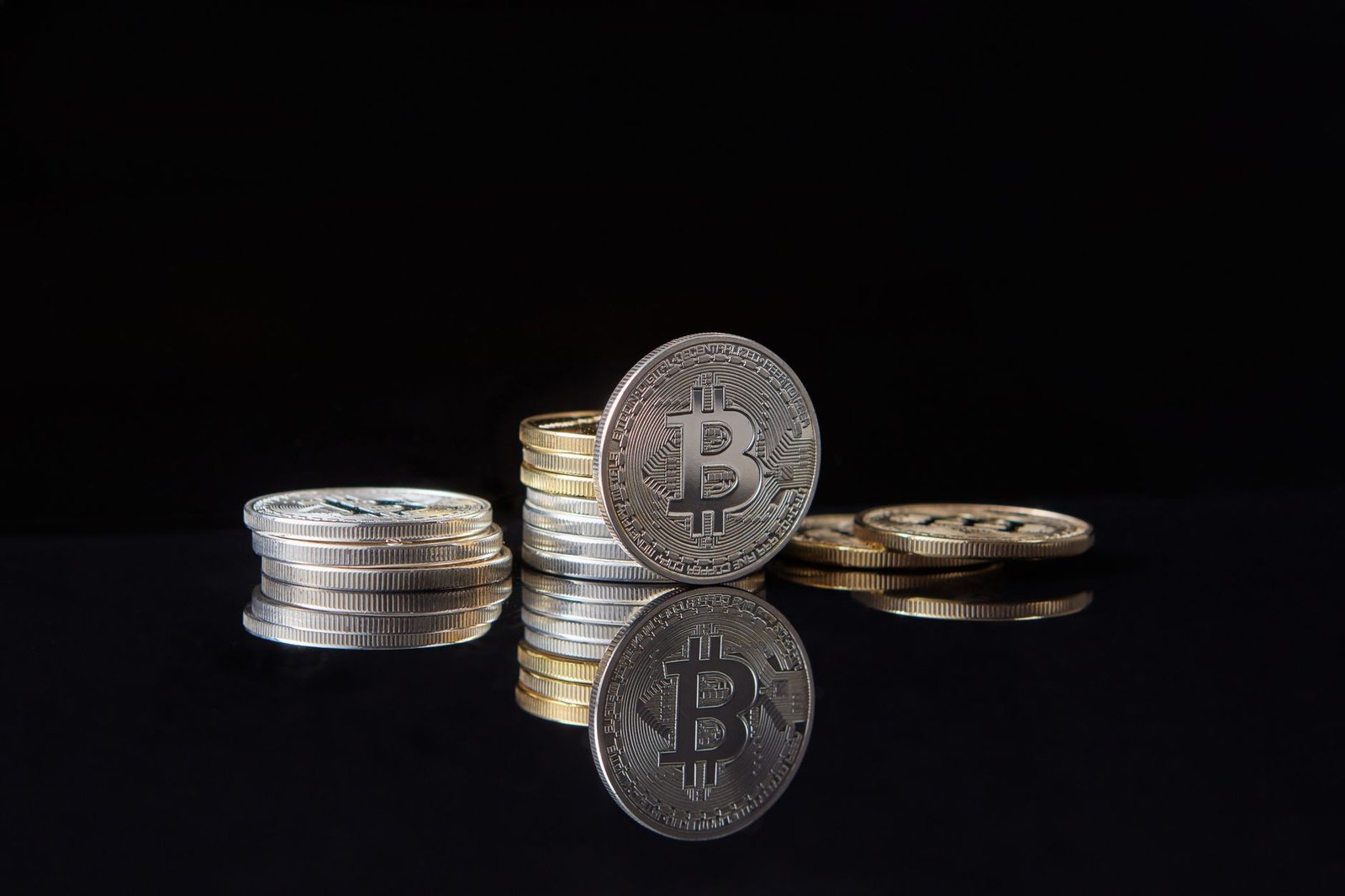 Silver bitcoins stacked on a reflective surface with a dark background, symbolizing cryptocurrency and digital wealth.
