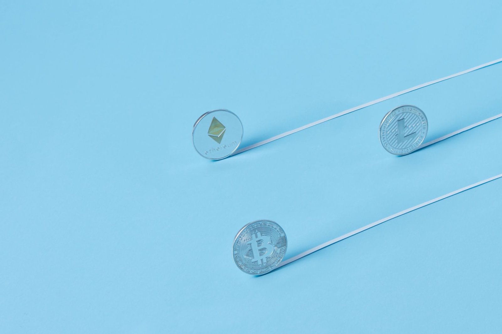 Minimalist image of Bitcoin, Ethereum, and Litecoin coins on a baby blue background.