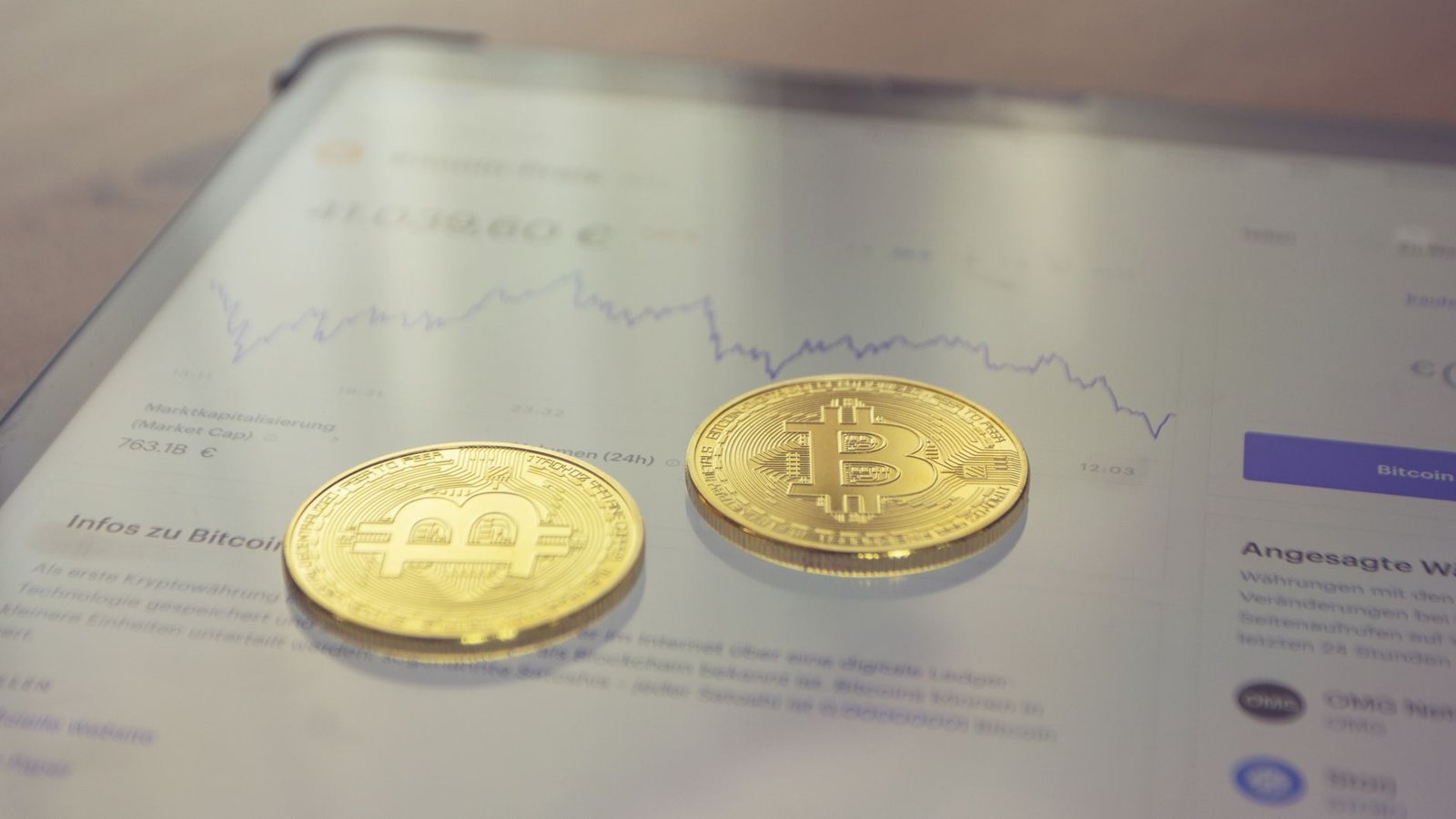 Close-up of two golden Bitcoin coins on a tablet screen displaying financial data.